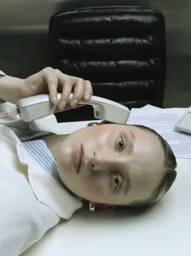 Woman lying on a white desk, phone receiver at her ear